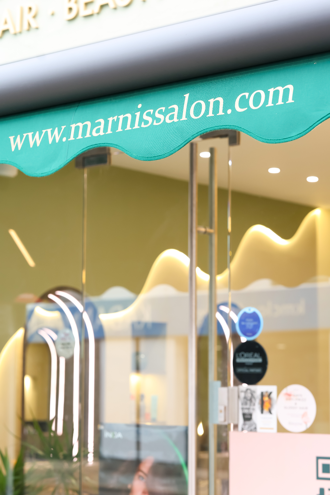 Marnis signature scalloped teal awning with marnissalon.live wordmark above the glass shopfront